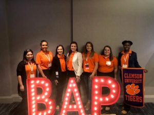 students and faculty pose behind lighted BAP sign