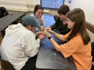 four students sitting at table building spaghetti and marshmallow structure