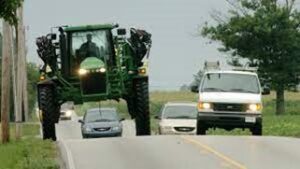 Rural roadway with sprayer traveling and multiple vehicles passing in the other lane. 