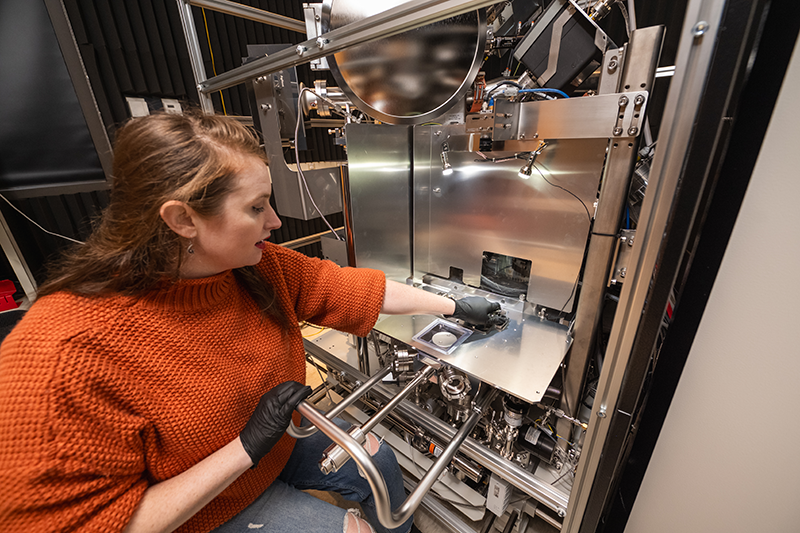 A women in an orange sweater sitting at a chrome machine.