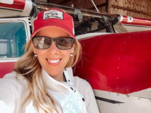 Kimberly Metris in hat and sunglases beside airplane fusselage.