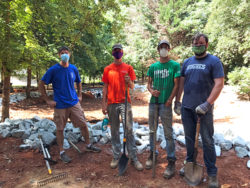 This picture shows four individuals standing with shovels with one of the completed swales behin them. 