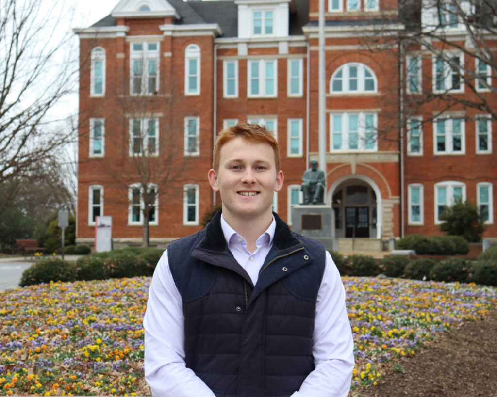 man with red hair outside in front of brick building.