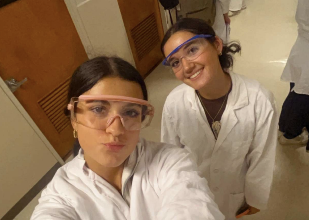 two grils taking a selfie with lab coats and lab goggles on.