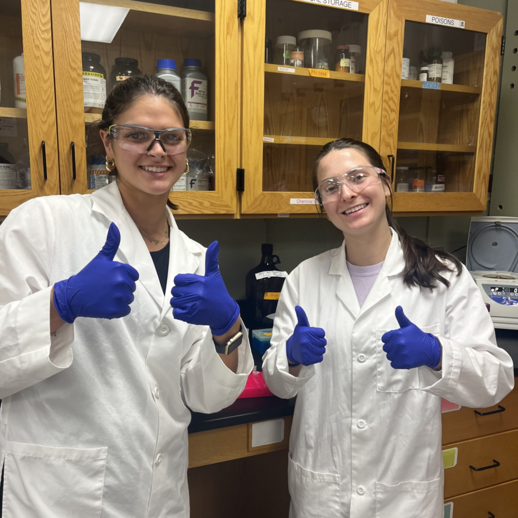 Two women in PPE with thumbs up smiling at camera,