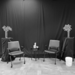 A Black and White photo of two chairs between two tiger lily plants on podiums.