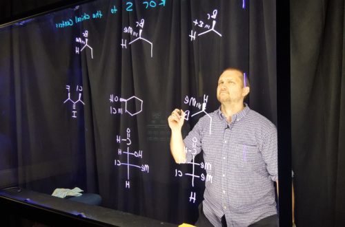 A man holding a marker and looking at chemistry formulas on the Lightboard.