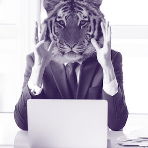 A tiger head on the body of a man wearing a business suit sitting in a video conference.