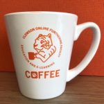 A picture of a white coffee mug with COFFEE logo printed in orange.