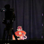 Camera pointing at a foam cutout of cartoon Clemson tiger leaning against a large orange letter C.