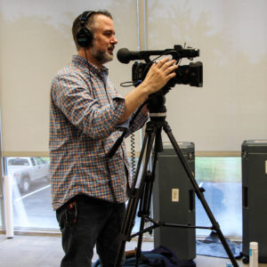 Man wearing headphones and filming something with a camera on a tripod.