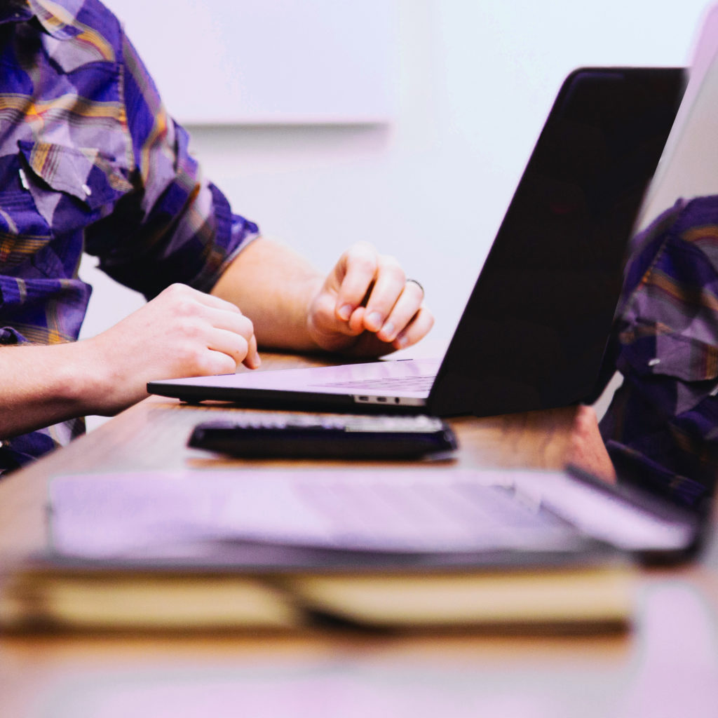 image depicts a person sitting at a table working on a laptop