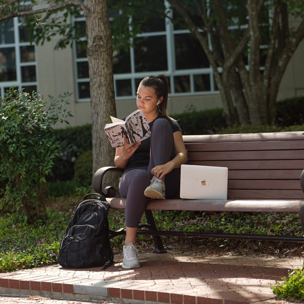 Image of a student reading a book on a bench on Clemson's campus.