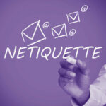 Person writing the word "netiquette" on a white board with drawn @ symbols and email envelopes