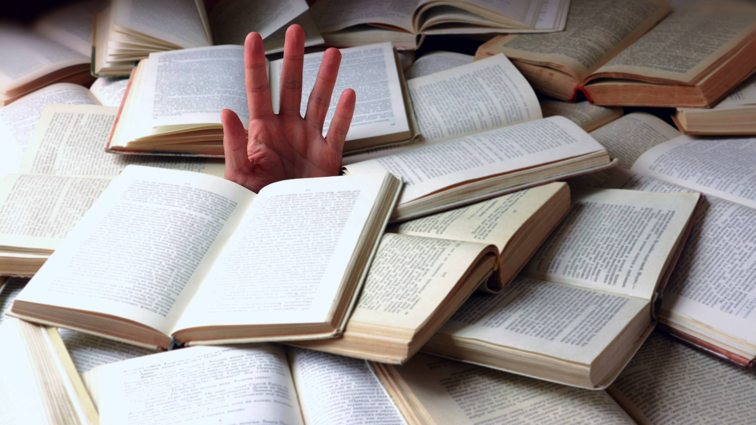A hand emerges from under a pile of open books