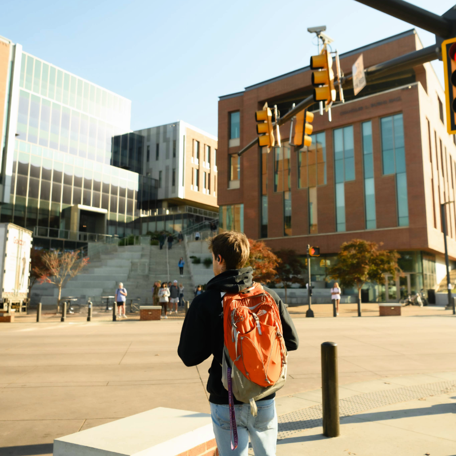 Image of a Clemson student crossing the street towards the Buisness Building wearing an orange backpack.