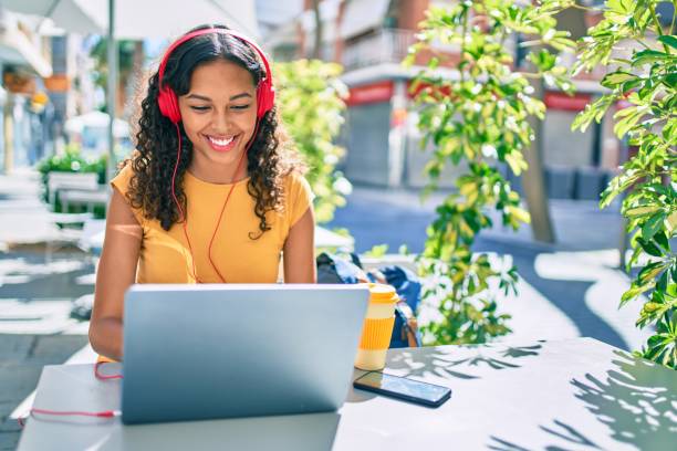 Image of a woman in a yellow shirt with red headphones working on a computer outside.