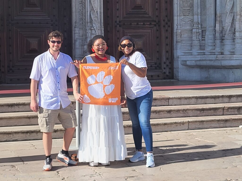 GE Next Engineers staff members Tyler Roland and Brittany Sanders-Bell, along with PEER & WISE Executive Director Serita Acker, smile for a photo while holding a Tiger Rag.