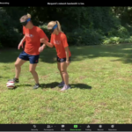 Two women wearing blindfolds playing soccer outside.