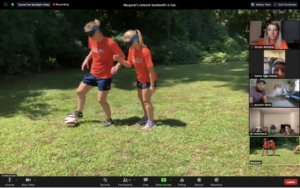 Two women wearing blindfolds playing soccer outside.