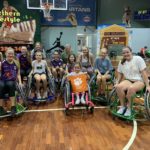 People posing in wheelchair basketball chairs at a gym in Brisbane, Australia.