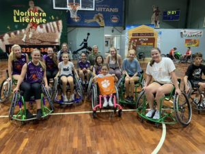 People posing in wheelchair basketball chairs at a gym in Brisbane, Australia.