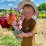 A toddler holding a bucket of flowers in the sun.