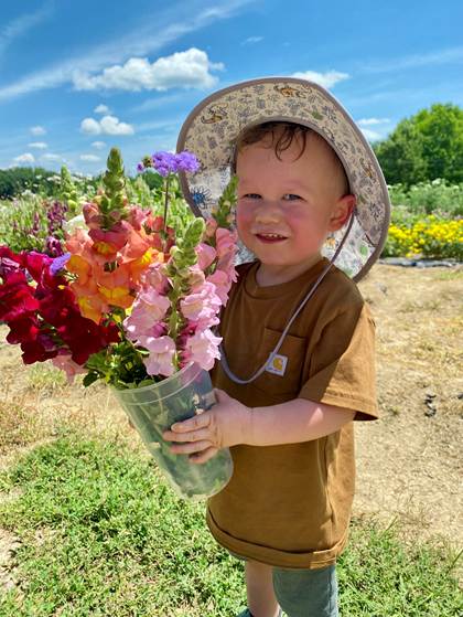 A toddler holding a bucket of flowers in the sun. 