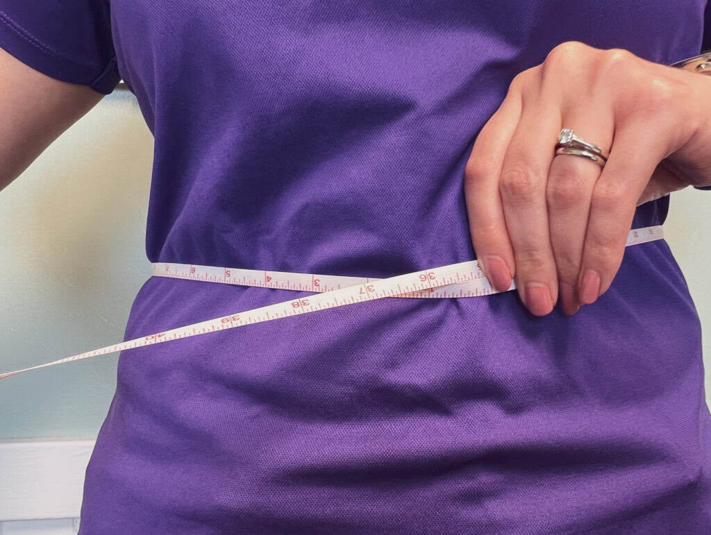 A person measuring their waist with a tape measure