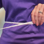 A person measuring their waist with a tape measure