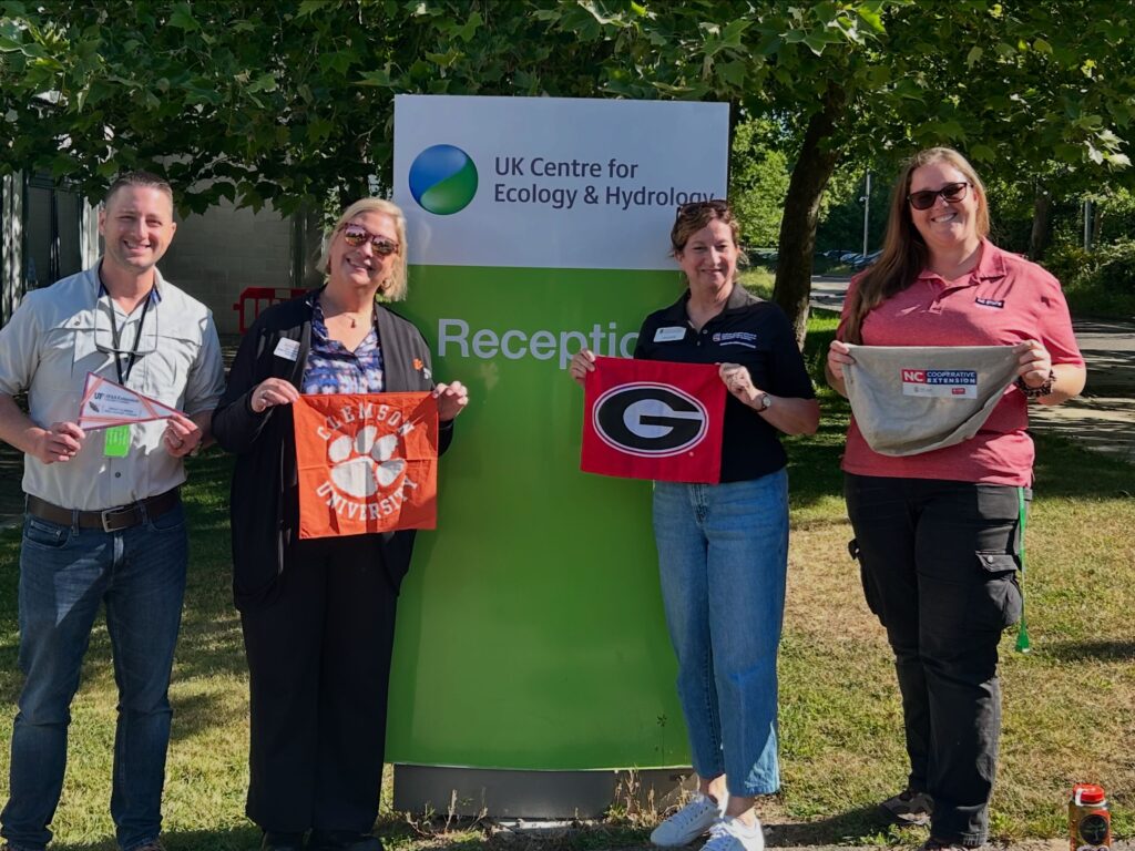 Extension agents from Florida SC, GA and NC holding their university flags in front of a sign at the UK Hydrology Lab