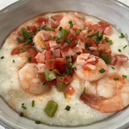 Grits topped with sauteed shrimp, canadian bacon, peppers, tomatoes, and chives