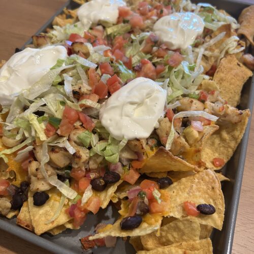 nacho chips topped with black beans, sour cream, cheese, pico de gallo, chicken, and lettuce