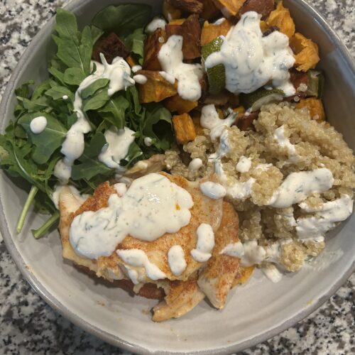 Grain bowl with fish, quinoa, greens, and roasted vegetables topped with a yogurt dill dressing
